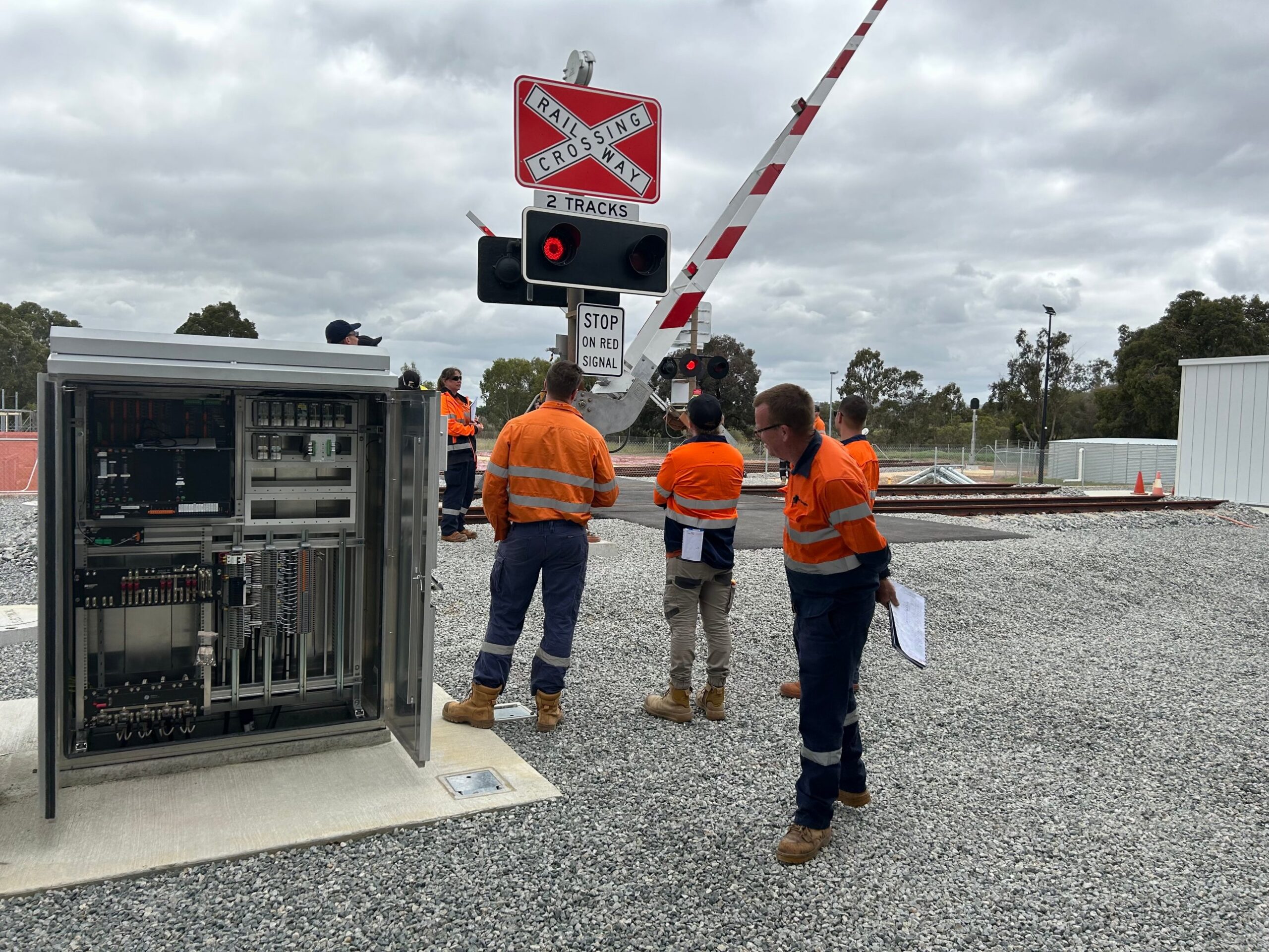 Industrial electricians working on rail signalling equipment at a level crossing